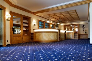 Une pièce spacieuse avec un grand comptoir d’accueil en bois, des étagères intégrées et une moquette à motifs.
