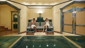 A spa area with a pool, two people sitting on a bench, and a door labeled "TOILET." - Schüle's Gesundheitsresort & Spa - Erwachsenenhotel (Oberstdorf)