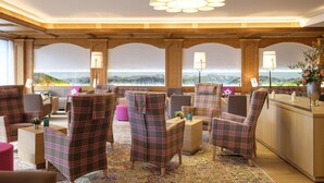 A cozy lounge area with plaid chairs, a wooden bar, and a view of mountains. - Schüle's Gesundheitsresort & Spa - Erwachsenenhotel (Oberstdorf)