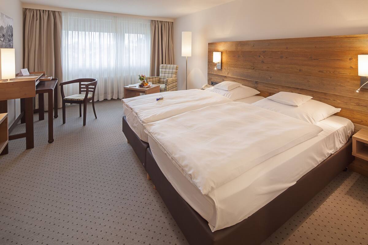 Ein Hotelzimmer mit einem großen Bett, einem Schreibtisch, einem Sessel und einem kleinen Tisch mit einer Lampe.