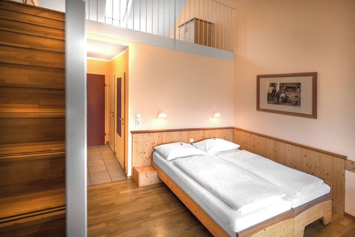 A single bed with a wooden headboard in a room with wooden flooring and a sloped ceiling.