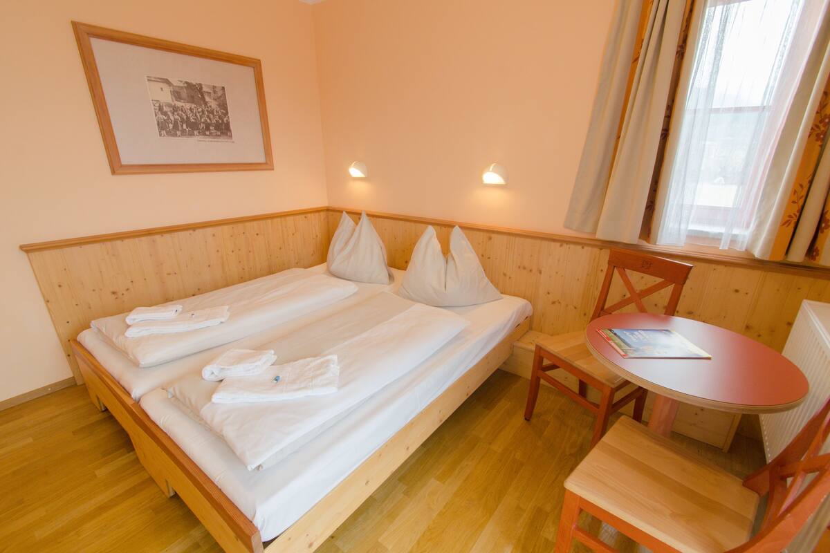 A room with a wooden bed, a small table, and a chair.