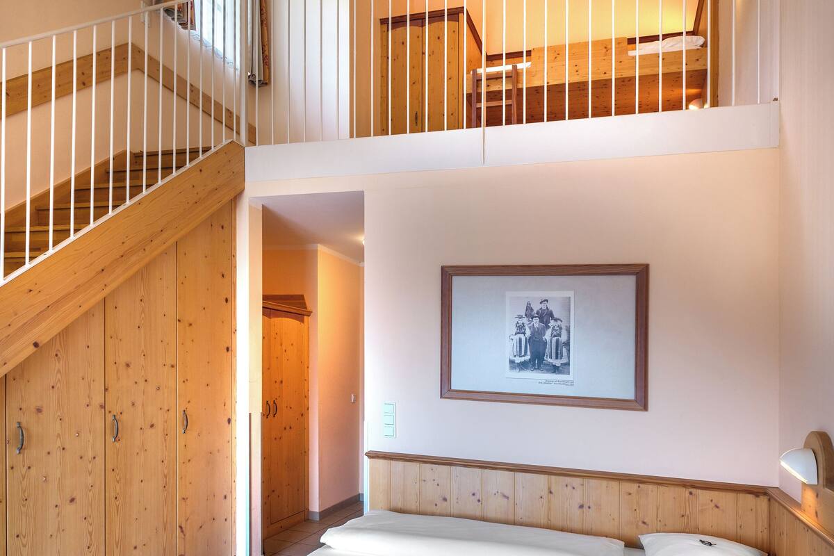 A hotel room with a wooden staircase, a bed with white linens, a framed picture on the wall, and a small table with a lamp.