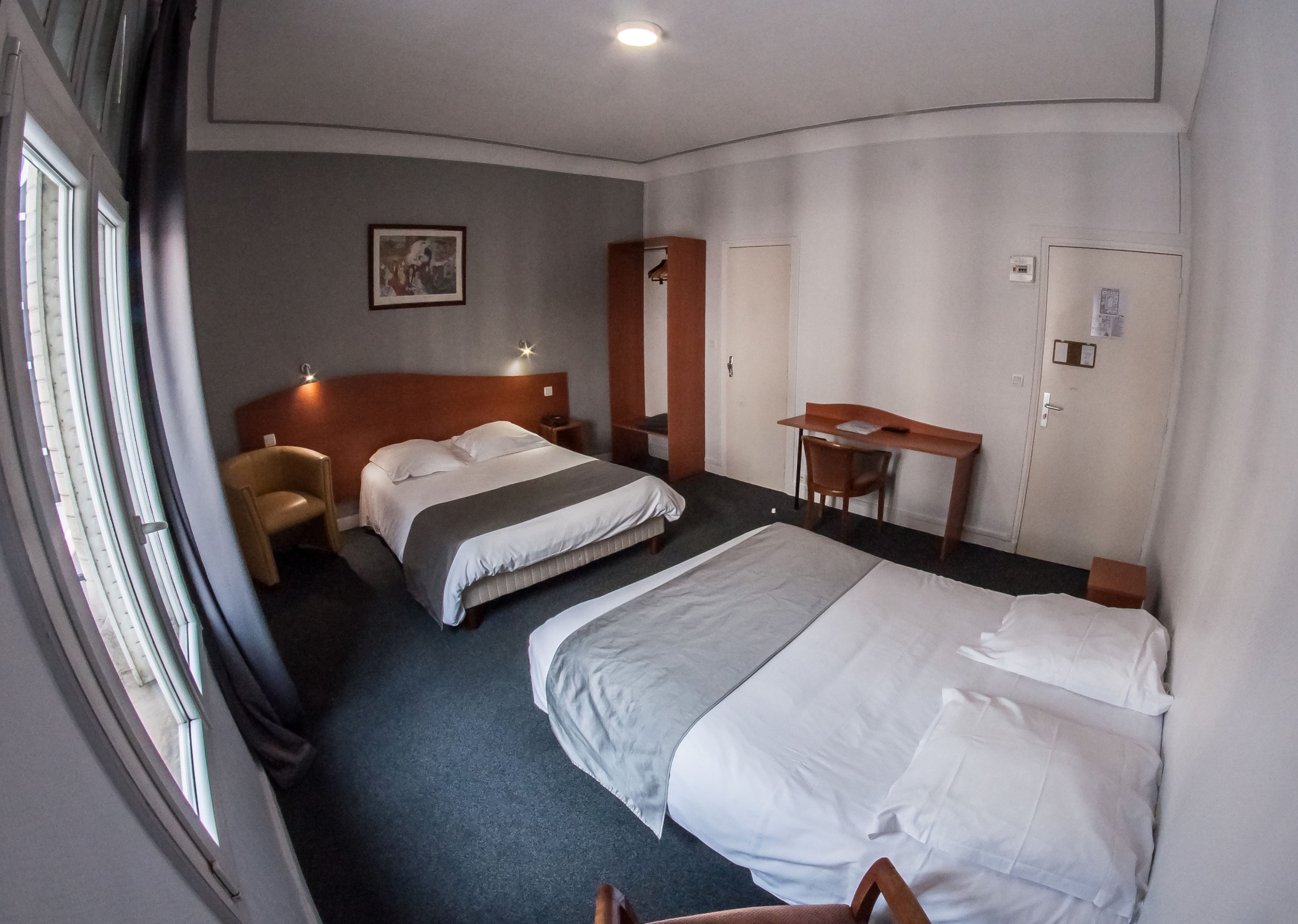 A hotel room with two beds, a desk, a chair, and a wardrobe.