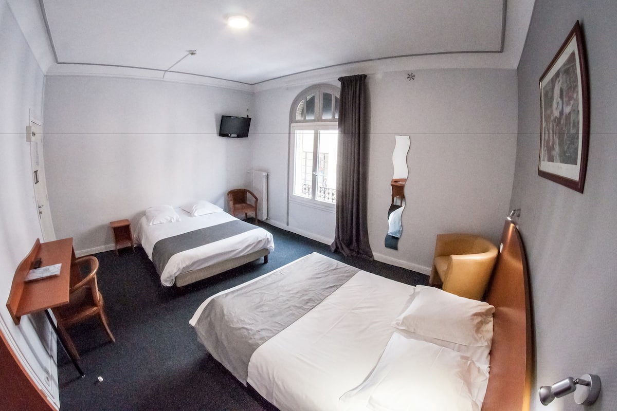 A hotel room with two beds, a desk, a chair, a television, a window with curtains, and a framed picture on the wall.