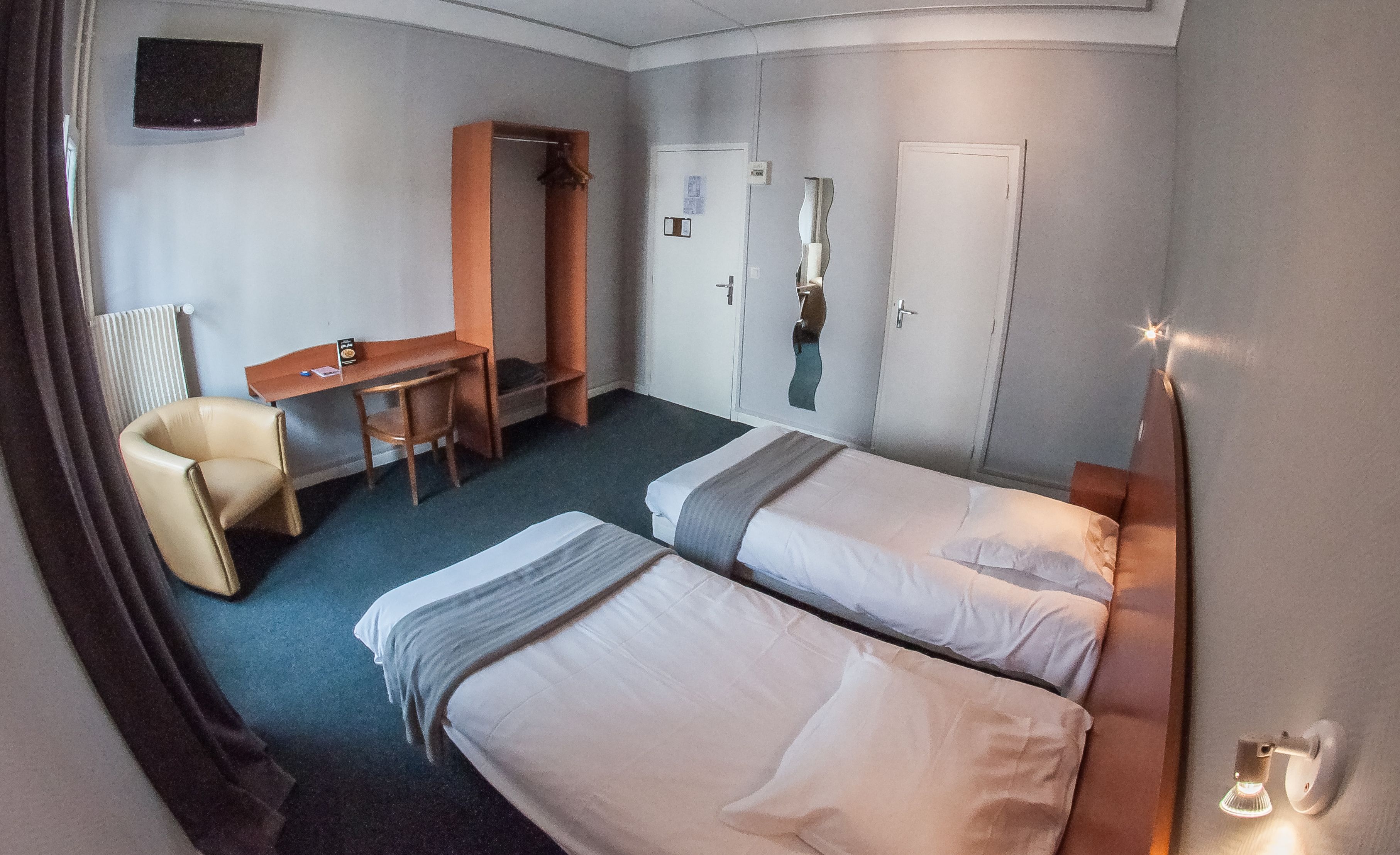 Une chambre d’hôtel avec deux lits, un bureau, une chaise et une armoire.