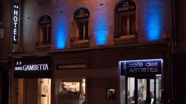 Un hotel llamado "Hotel Gambetta" con un letrero llamativo y un café llamado "café des ARTISTES" al otro lado de la calle.