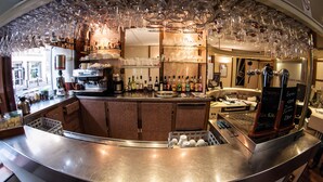 Zona de bar con mostrador curvo, estanterías con botellas y un colgador para copas.