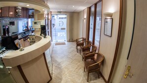 Un hall de hotel con mostrador de recepción, zona de bar y varias sillas de madera.