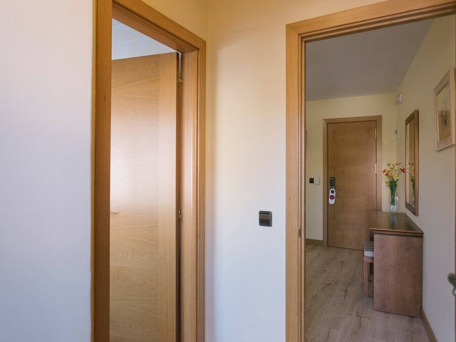 Un couloir avec des portes en bois, un petit bureau orné d’un vase de fleurs et un miroir accroché au mur.