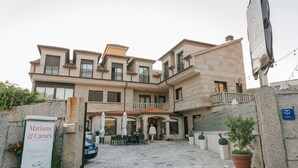 A hotel with a traditional facade, outdoor seating, and a sign for 'Mariscos & Carnes'. - O Castro (O Grove)