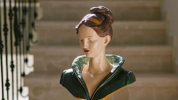 Escultura tipo busto sobre un pedestal en una zona de escaleras.