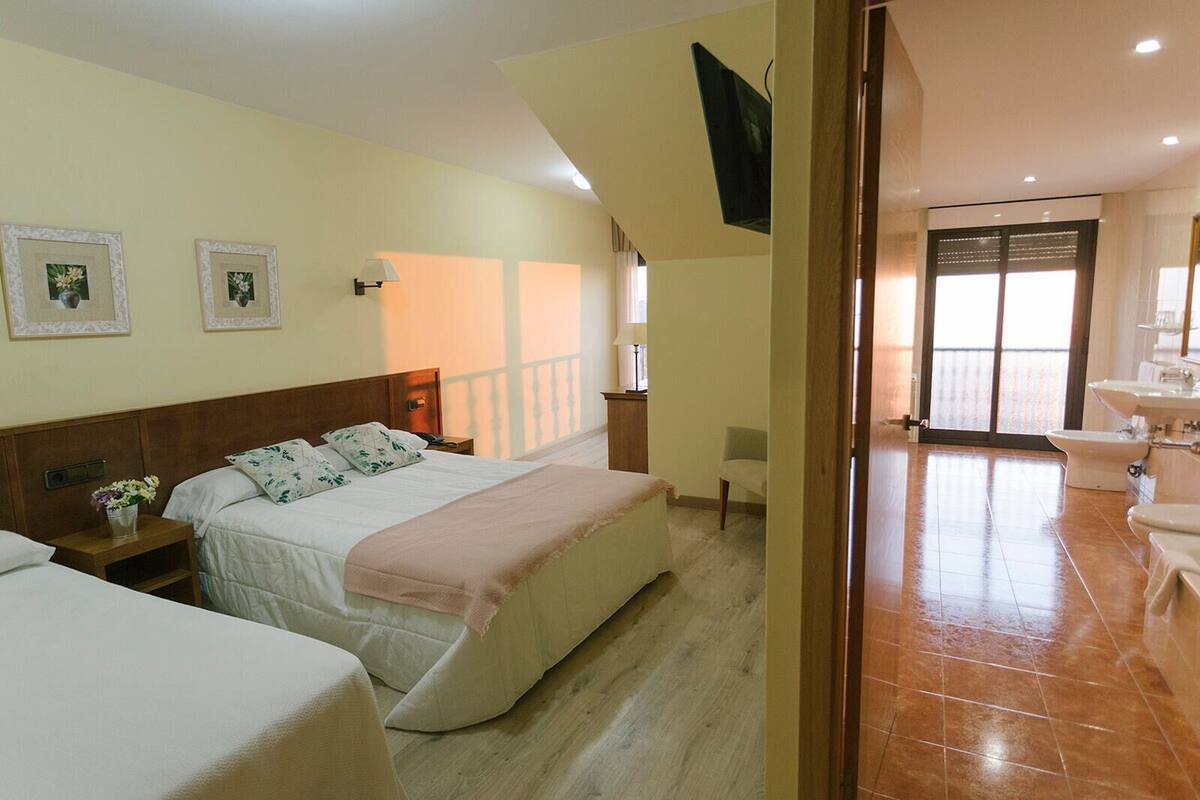 Habitación de hotel con dos camas, un baño con lavamanos e inodoro, y un balcón con vistas.