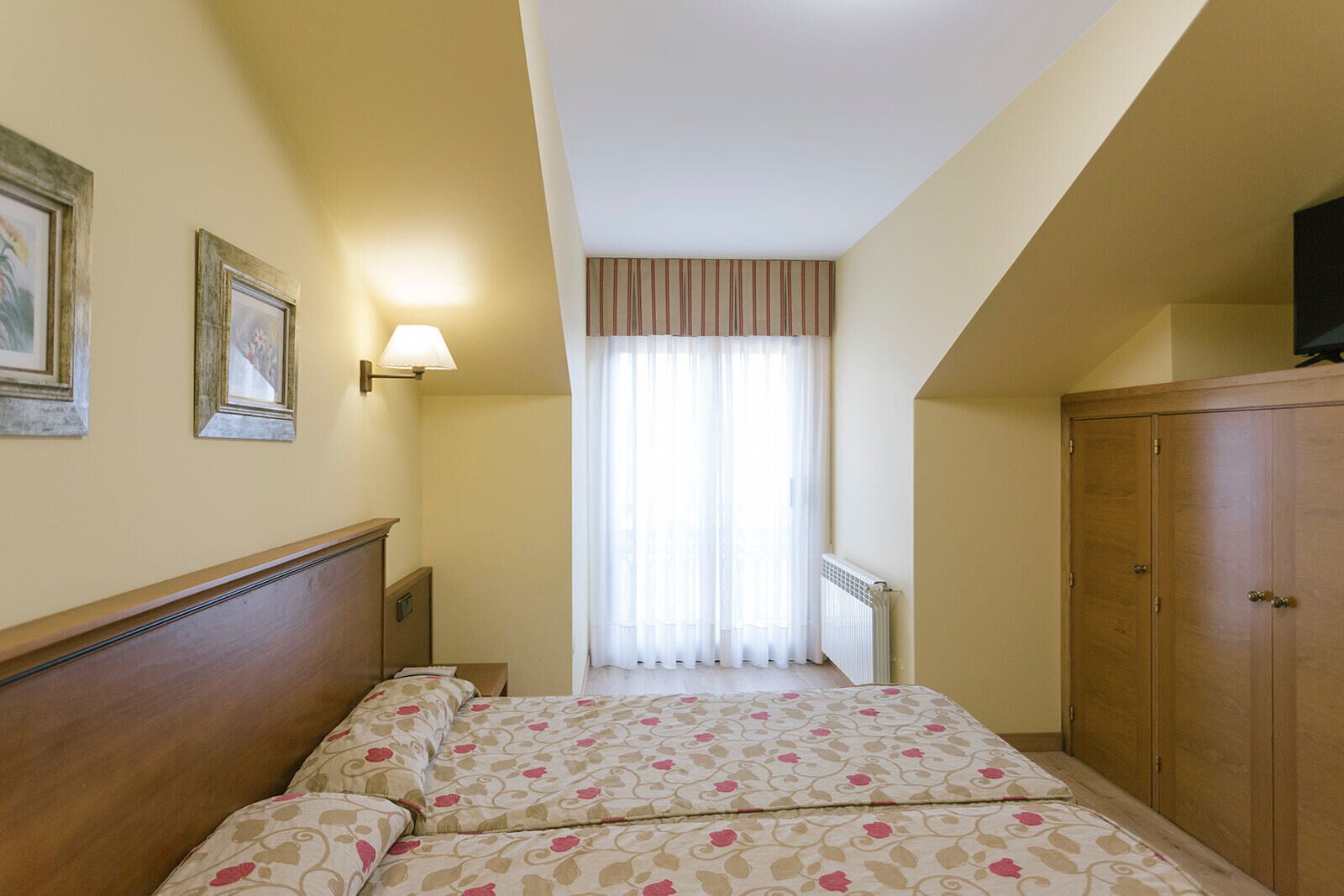 Een hotelkamer met een bed, een kledingkast, een radiator en een raam met gordijnen.