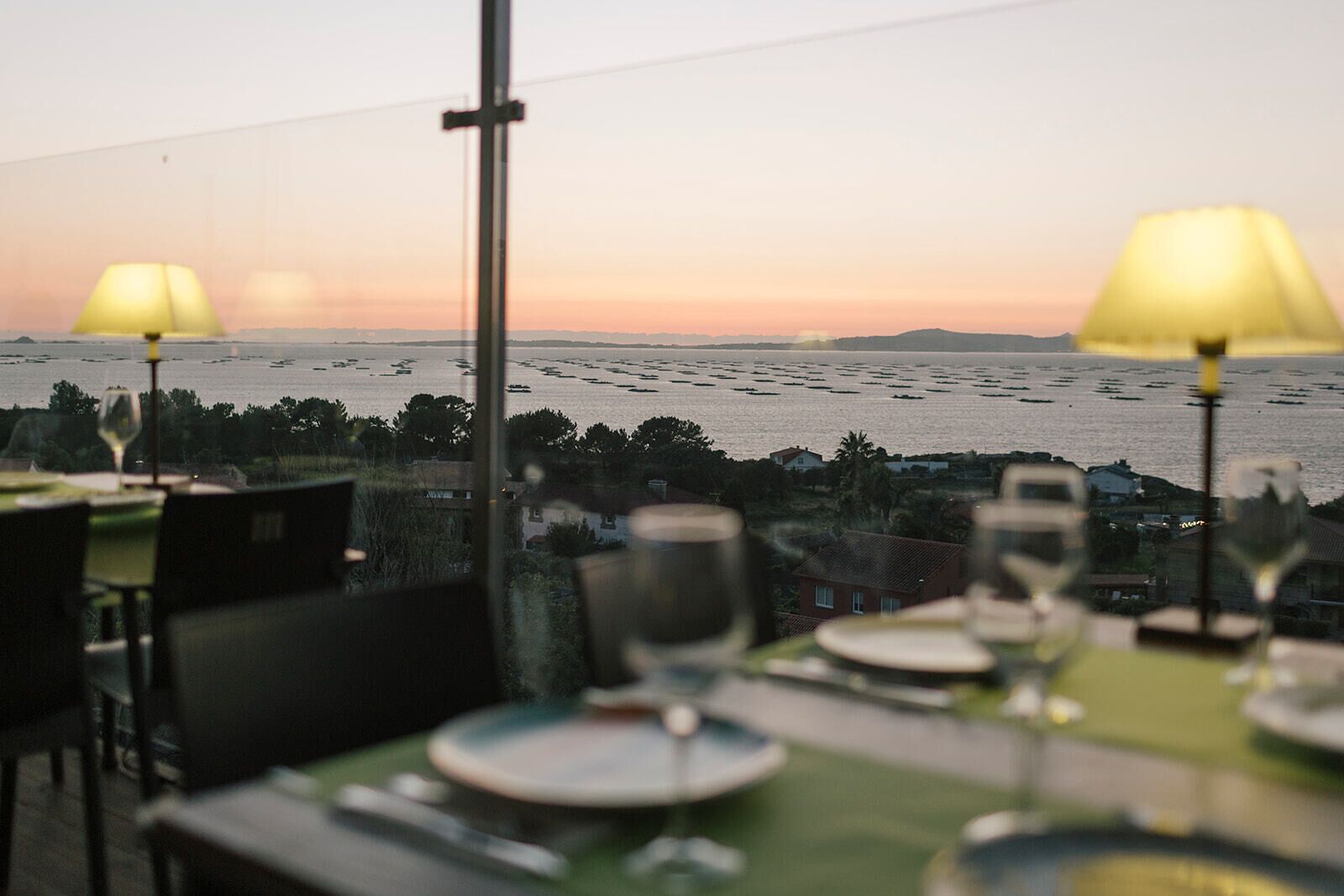 Mesa posta para refeição com vista para um corpo d'água e terra distante ao pôr do sol.