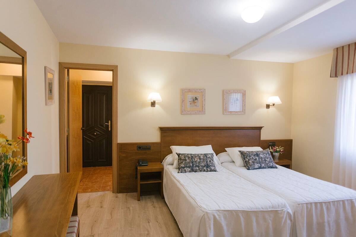 Una habitación de hotel con una cama doble, mesitas de noche, una puerta de madera y lámparas fijadas a la pared.