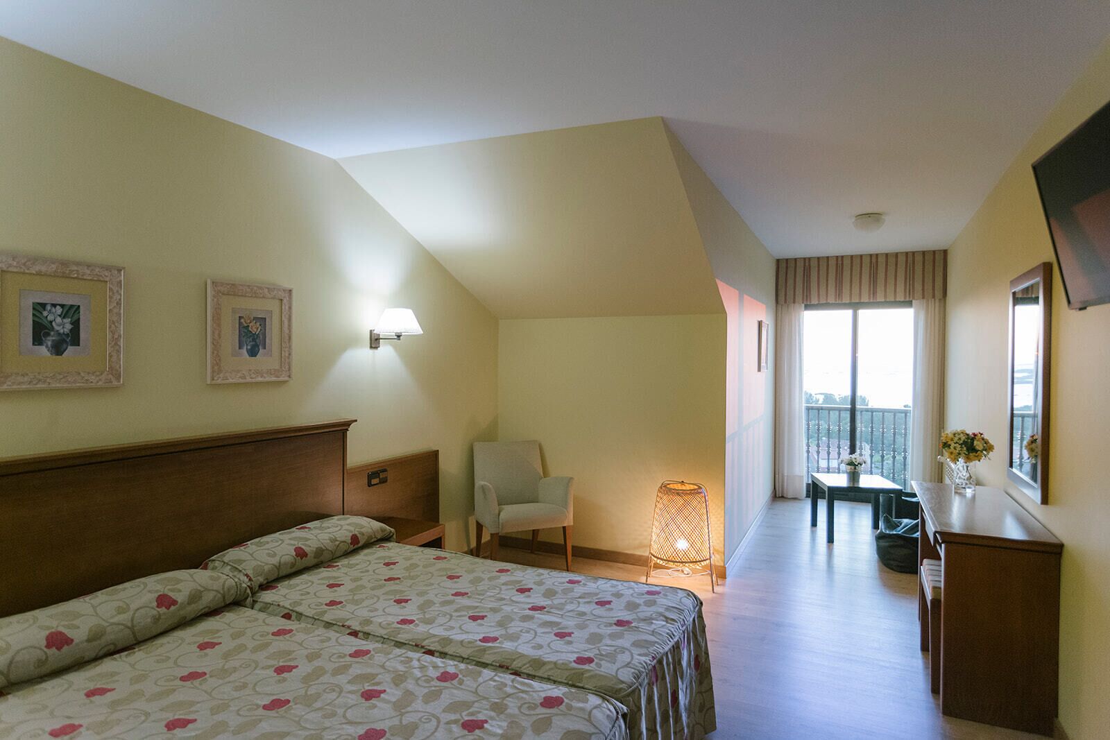 Habitación de hotel con cama, una silla, escritorio y balcón con vistas.