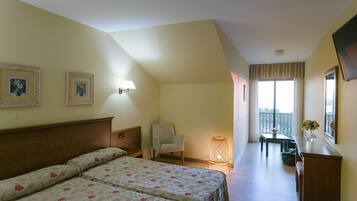 Habitación de hotel con cama, una silla, escritorio y balcón con vistas.