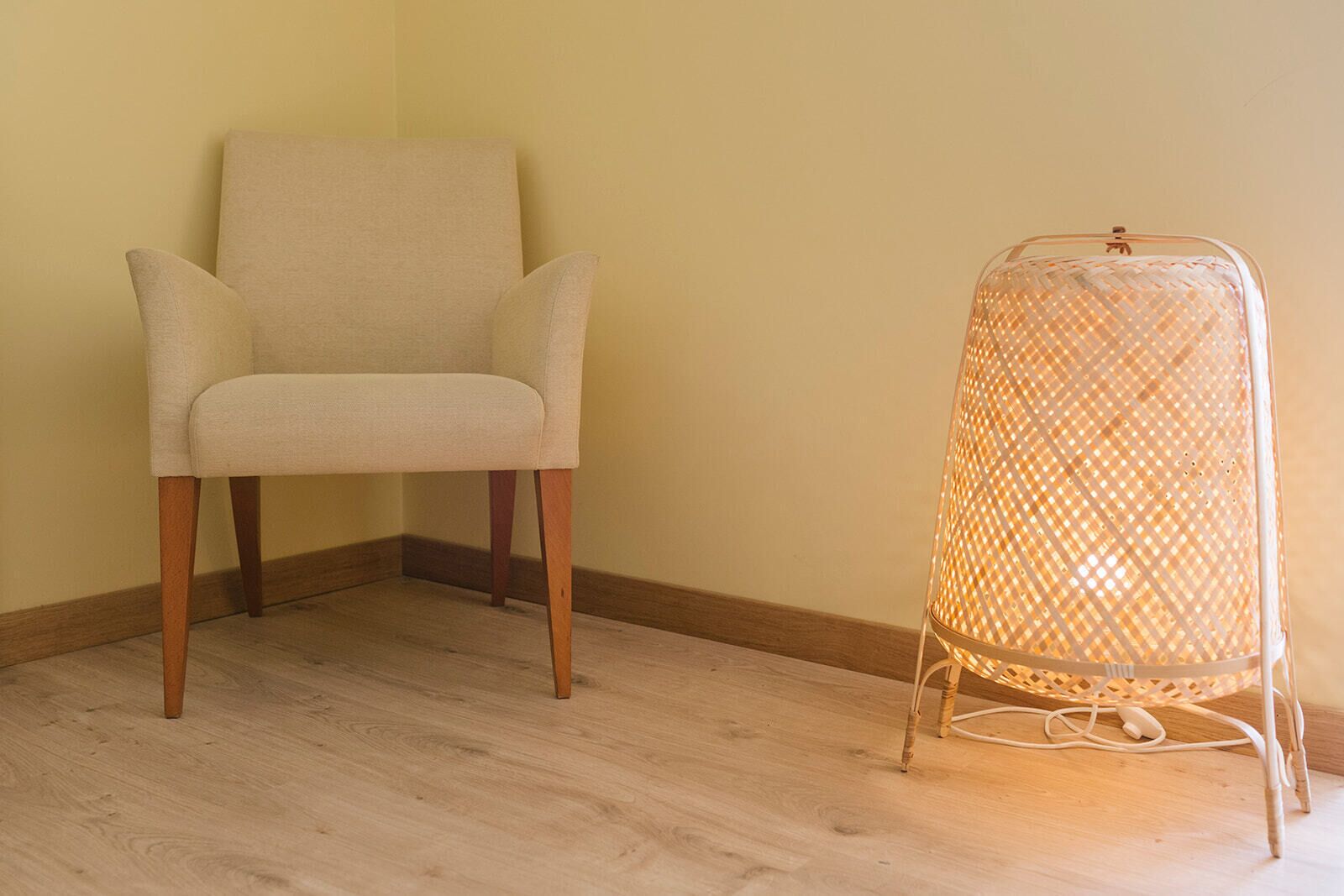 Een stoel en een vloerlamp in een hoek van een kamer met houten vloeren en een effen muur.