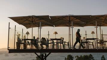 An outdoor dining area with tables and chairs under large umbrellas, overlooking a body of water.