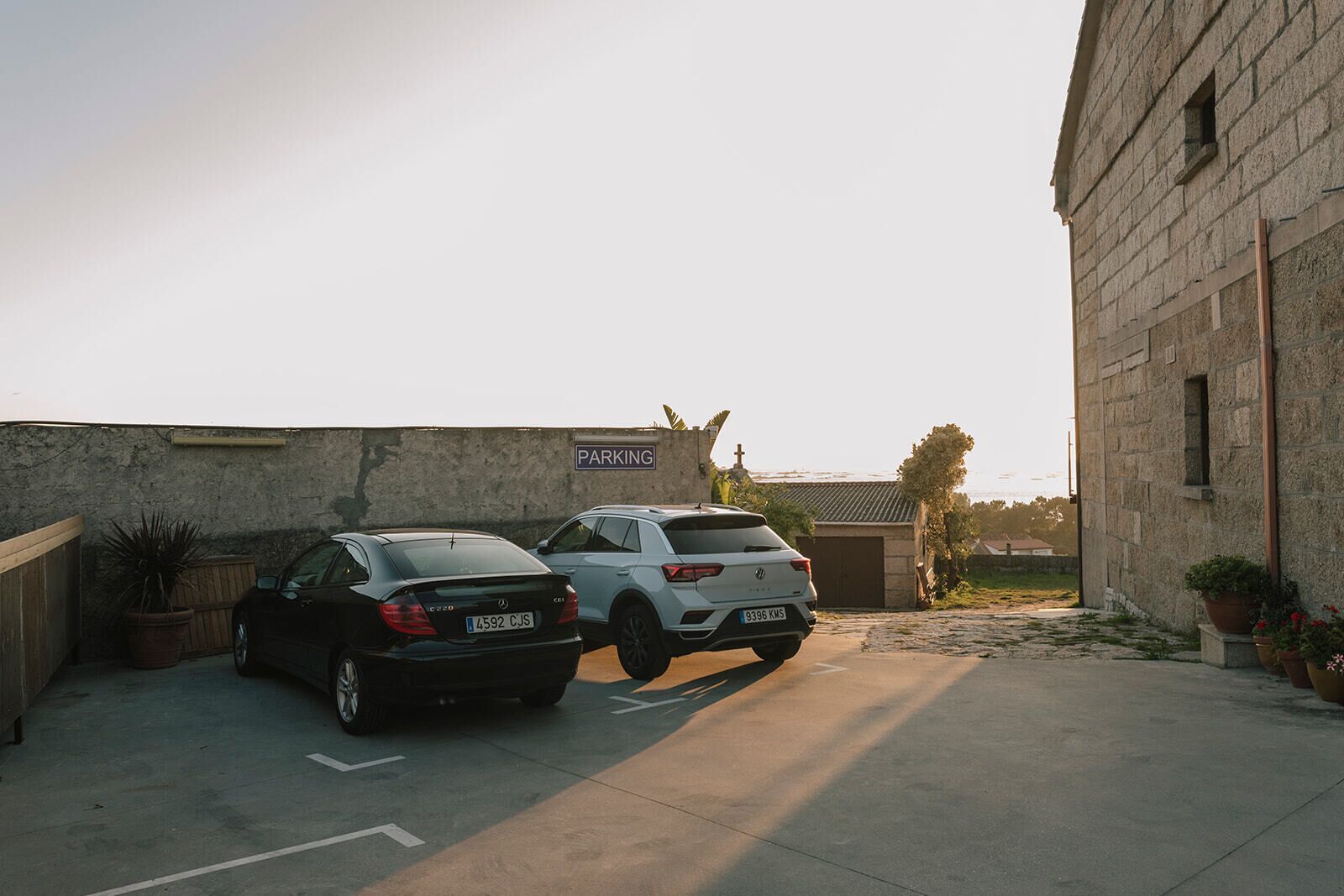Un espace de stationnement avec deux voitures, un bâtiment en pierre et un panneau indiquant qu’il s’agit d’un parking.