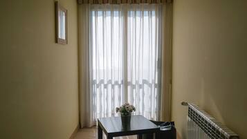 Une petite pièce étroite, avec une table, un radiateur et une fenêtre ornée de rideaux légers.