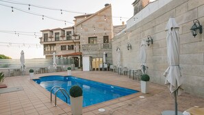 A swimming pool with a tiled deck, surrounded by outdoor seating and umbrellas, with a building in the background. - O Castro (O Grove)