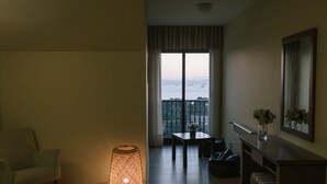 A hotel room with a balcony, a table with chairs, a lamp, a chair, a dresser, and a mirror. - O Castro (O Grove)