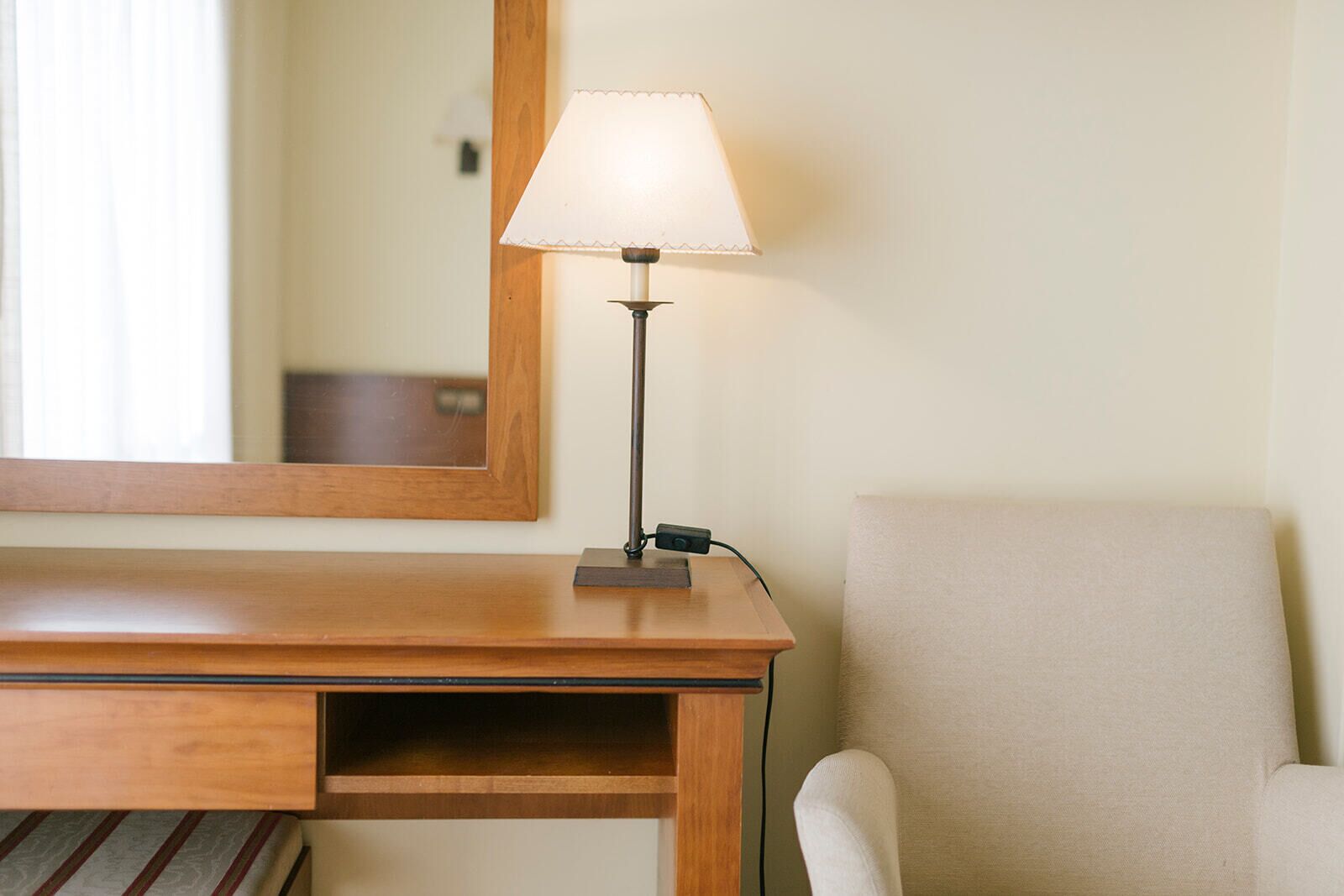 A wooden desk with a lamp, a chair, and a mirror on the wall.