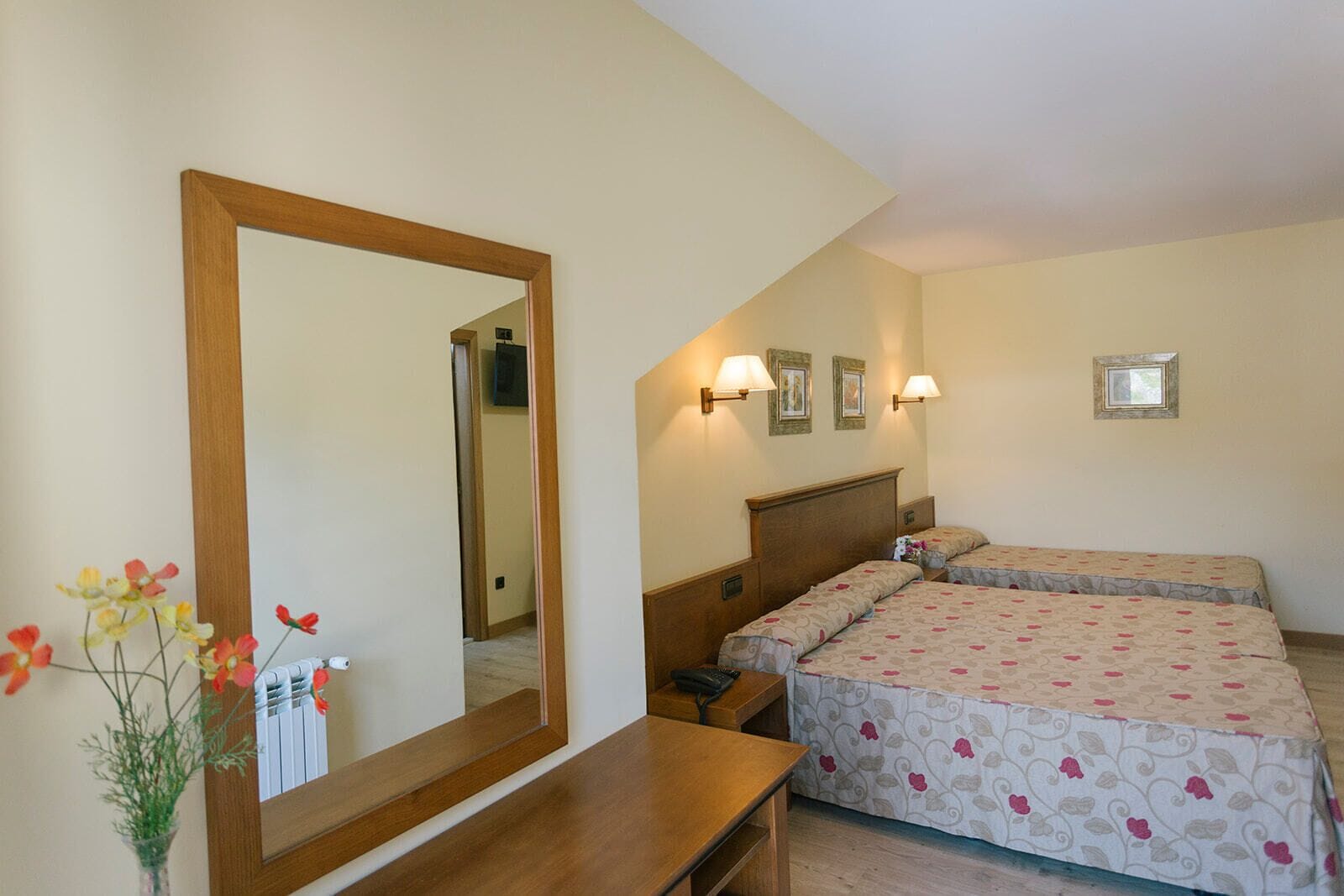 A hotel room with two beds, a large mirror, bedside lamps, a wooden desk, and a vase with flowers.