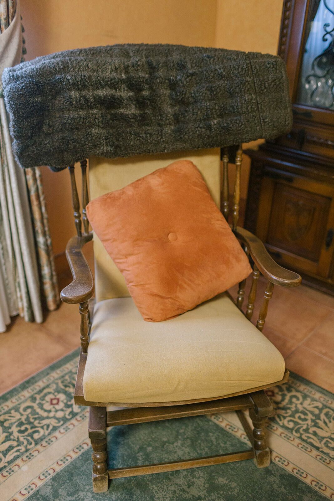 Une chaise recouverte d’un tissu foncé et texturé, agrémentée d’un seul coussin orange.