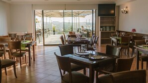 A restaurant with multiple tables and chairs, a large glass door leading outside, and a bar area with shelves of glasses. - O Castro (O Grove)