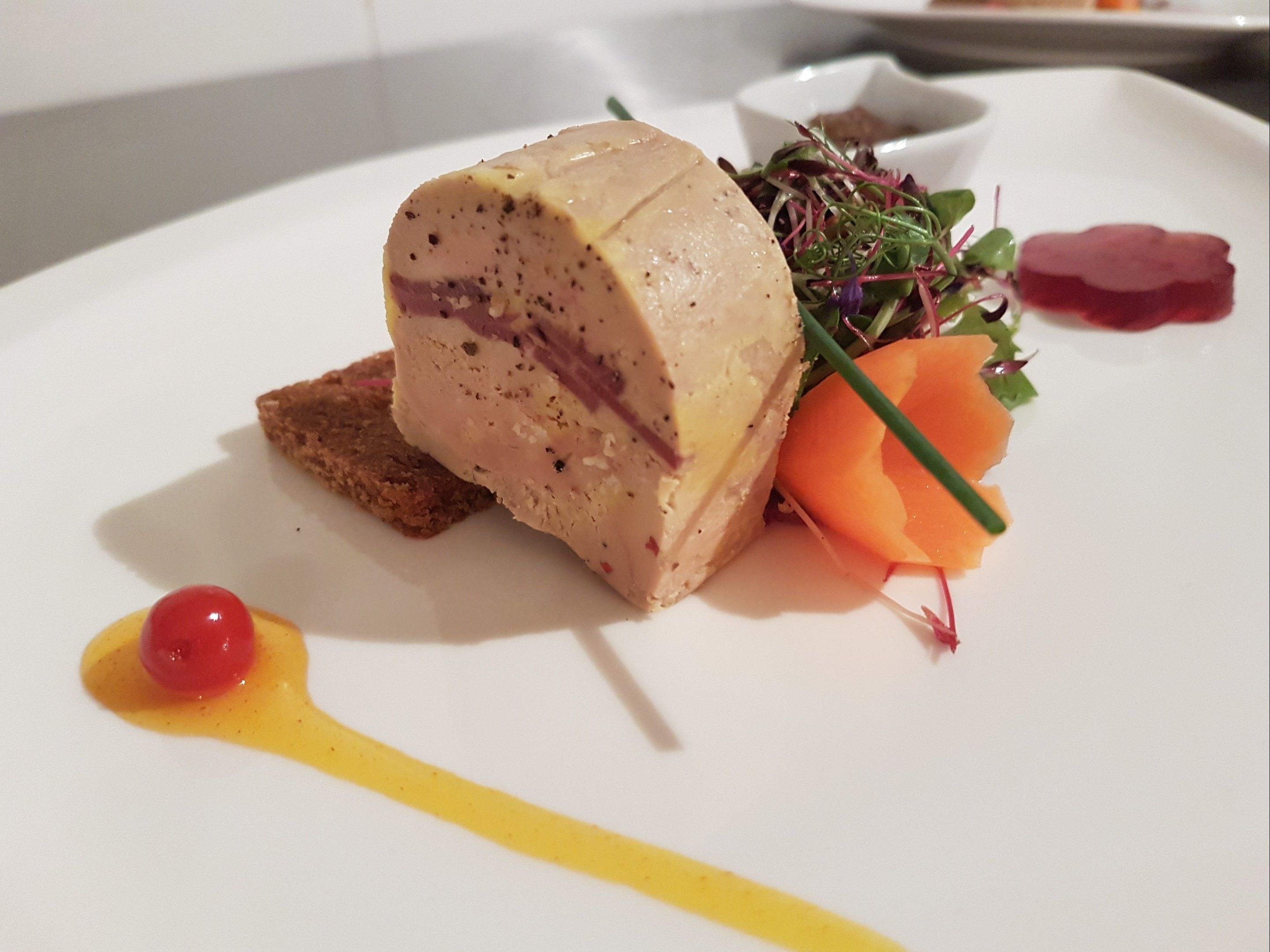 En tallerken med kødret, en lille skål med grønt, en gulerodsskive og en klat sauce.