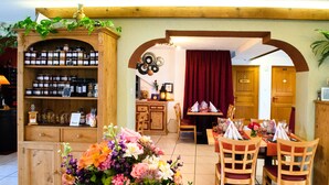 A dining area with wooden furniture, a flower arrangement, and a shelf with jars. - Rêves Gourmands (Vernayaz)