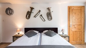 A double bed with white linens and two pillows, a wooden door, and brass instruments mounted on the wall. - Rêves Gourmands (Vernayaz)