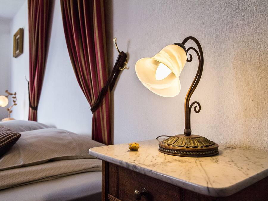 A bed with pillows, a nightstand with a lamp, and a wall with curtains.