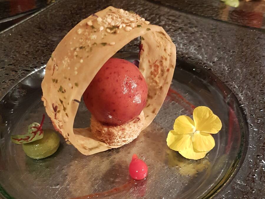 A dessert with a spherical red item, a yellow flower, and a red spherical decoration on a glass plate.