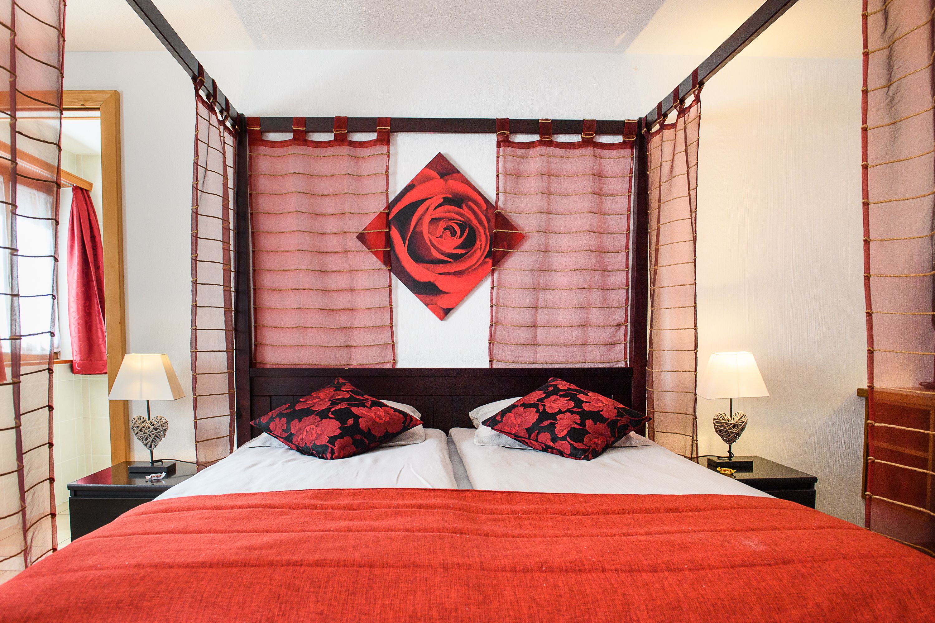 Habitación de hotel con una cama grande, dos mesitas de noche con lámparas, un adorno en la pared y una cortina roja.