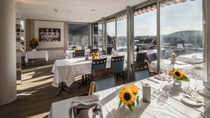 A dining area with tables set for service, large windows offering a city view, and a framed picture on the wall. - Hotel Roter Turm (Solothurn)