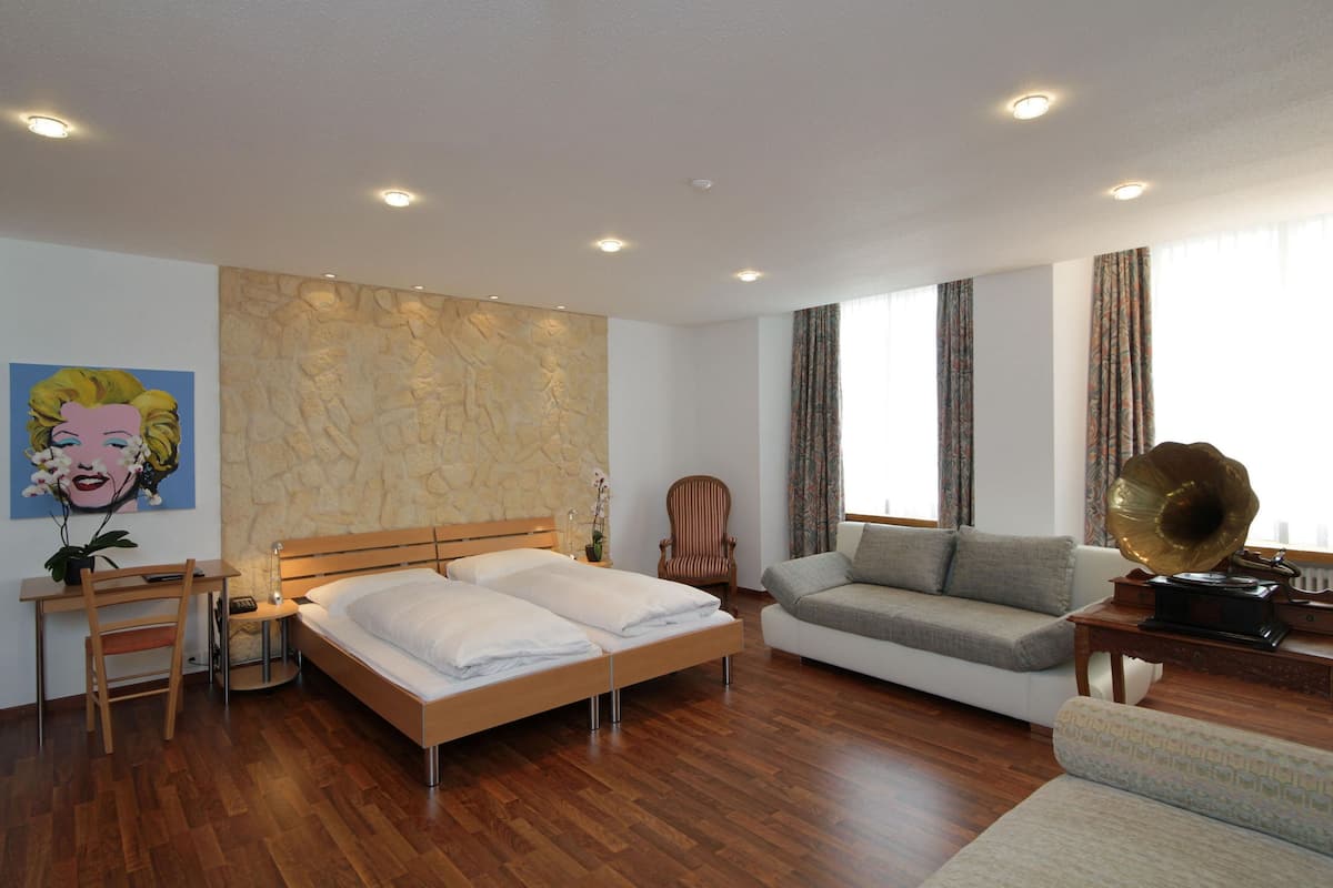 A modern bedroom with a large bed, a sofa, a desk, and a wall-mounted stereo.