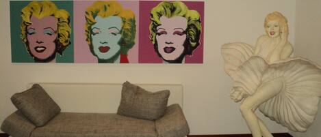 Una sala de estar con un sofá blanco, tres retratos de arte pop en la pared y una estatua de mujer.