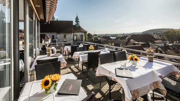 An outdoor dining area with tables and chairs, a view of a historic building, and a clear sky. - Hotel Roter Turm (Solothurn)