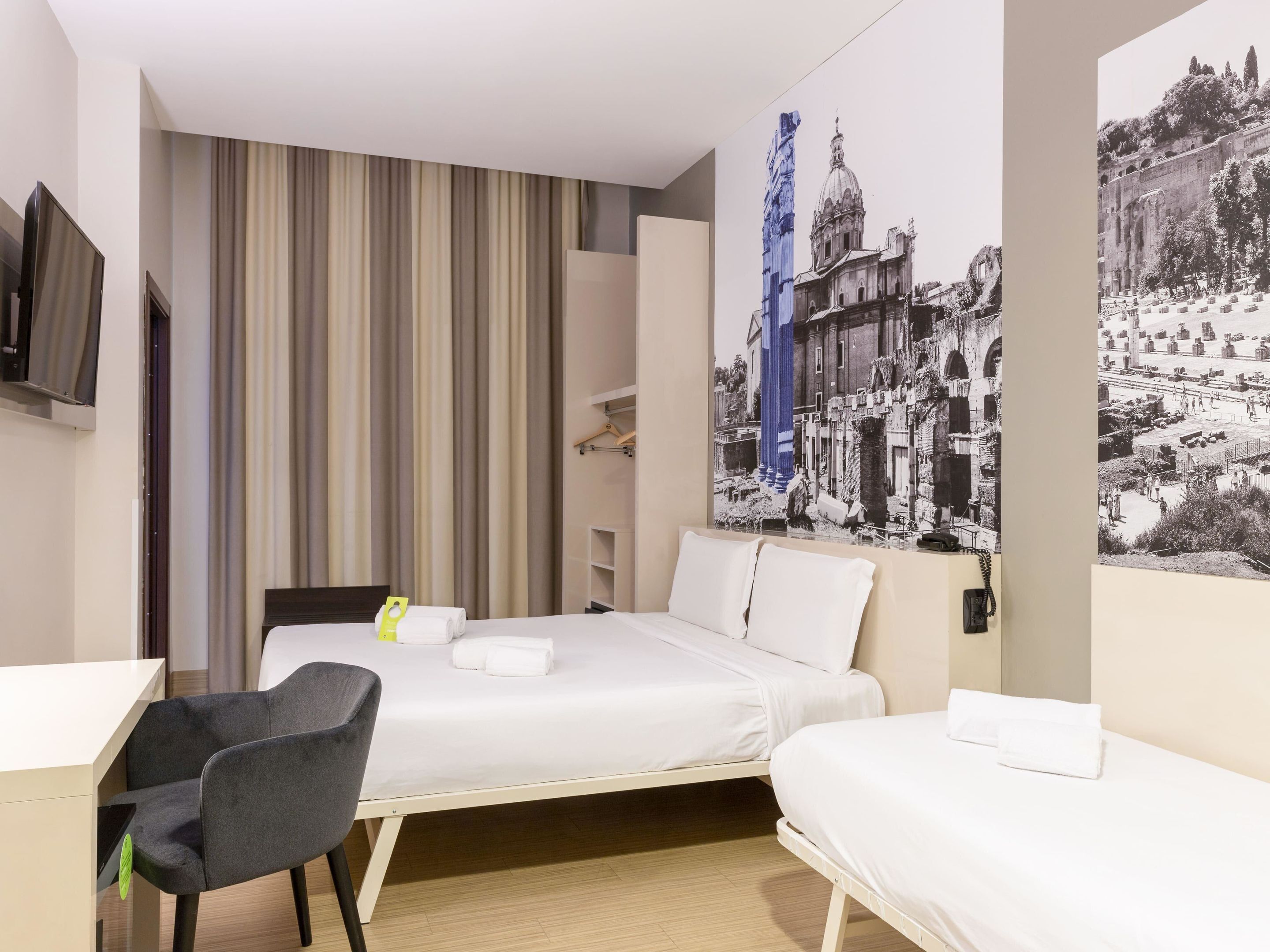 Una camera d'albergo con un letto, una scrivania, una sedia, una TV e un grande murale.