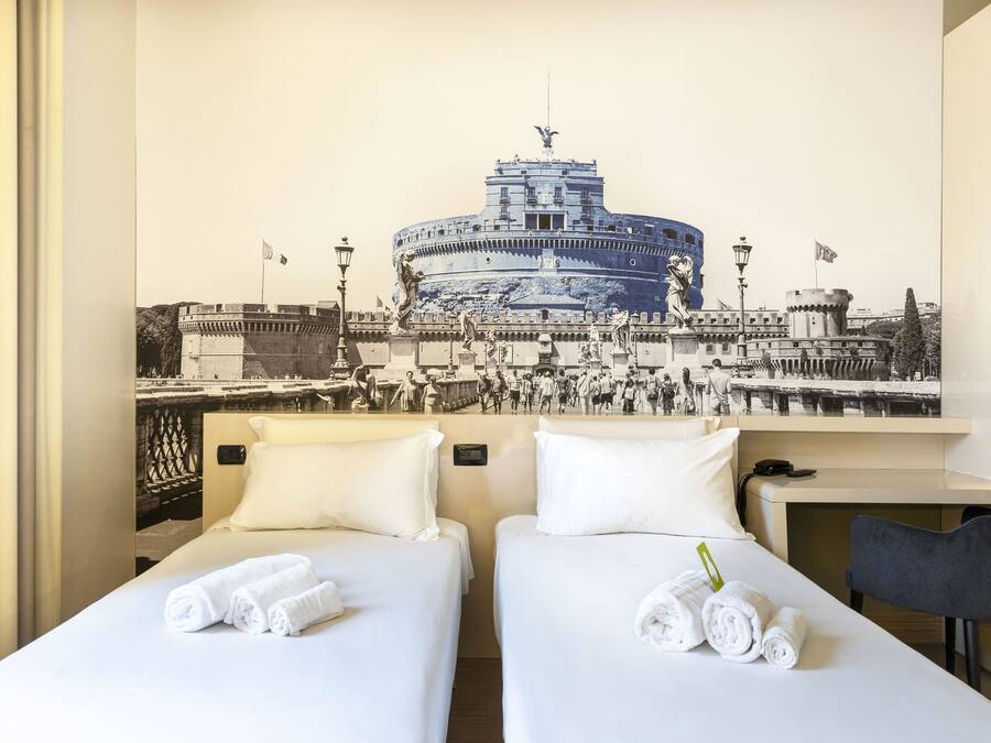 Ein Hotelzimmer mit zwei Betten, weißen Leinentüchern und Handtüchern. An der Wand hängt ein großes Schwarz-Weiß-Foto eines historischen Gebäudes.