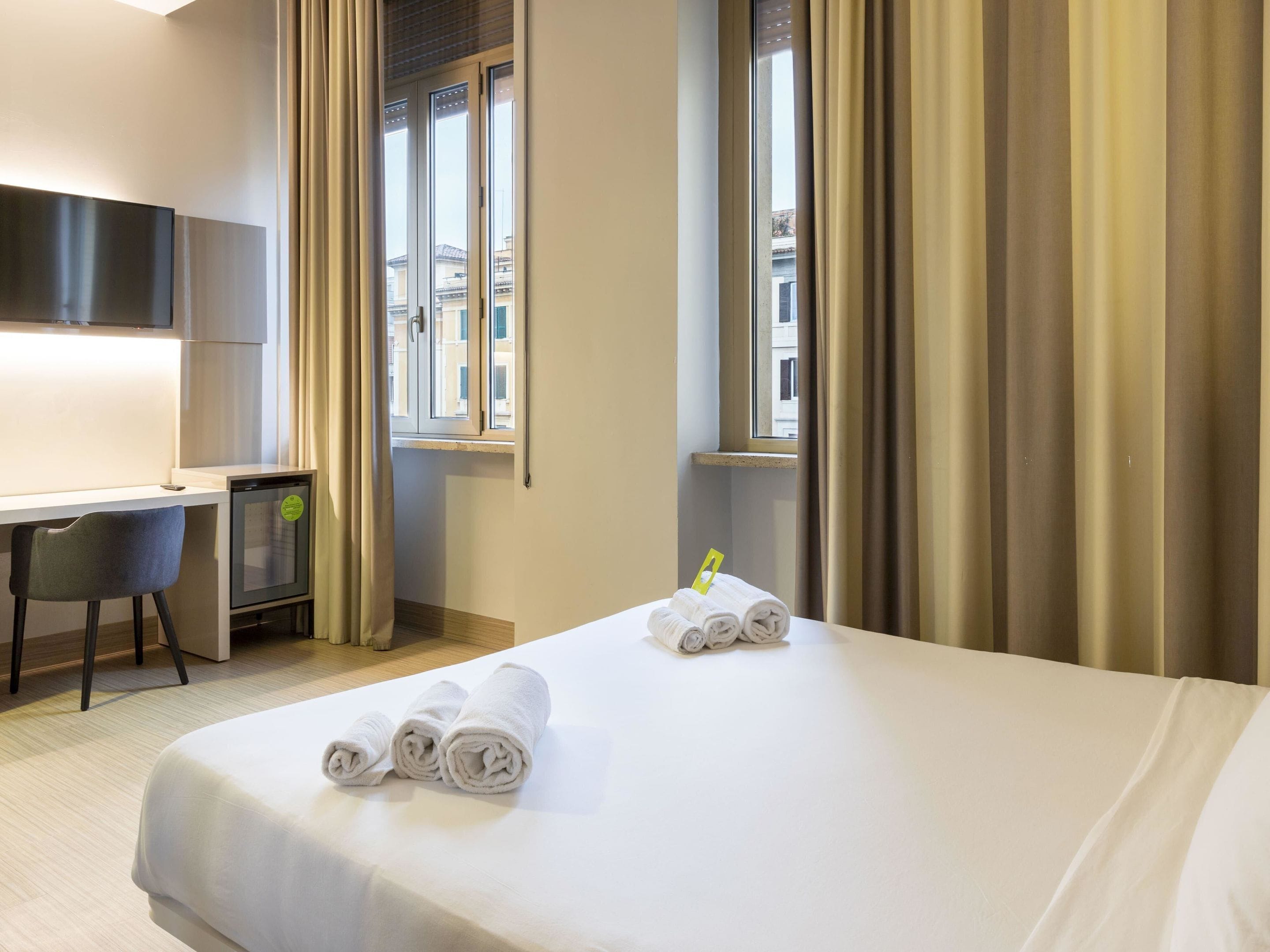Ett hotellrum med en säng, ett skrivbord, en stol och en tv.