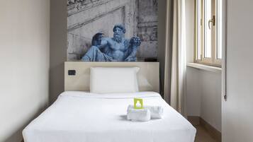 Ein Hotelzimmer mit Bett, weißer Bettwäsche, einem Wandbild einer klassischen Skulptur, einem Fenster mit Vorhängen und einem Nachttisch mit einem grünen Gegenstand.