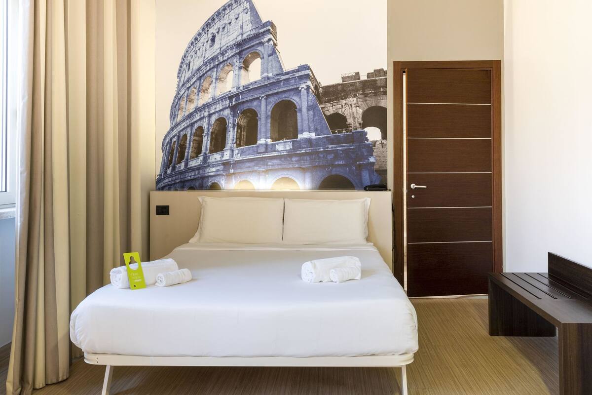 A hotel room with a bed, a wall-mounted phone, and a door.