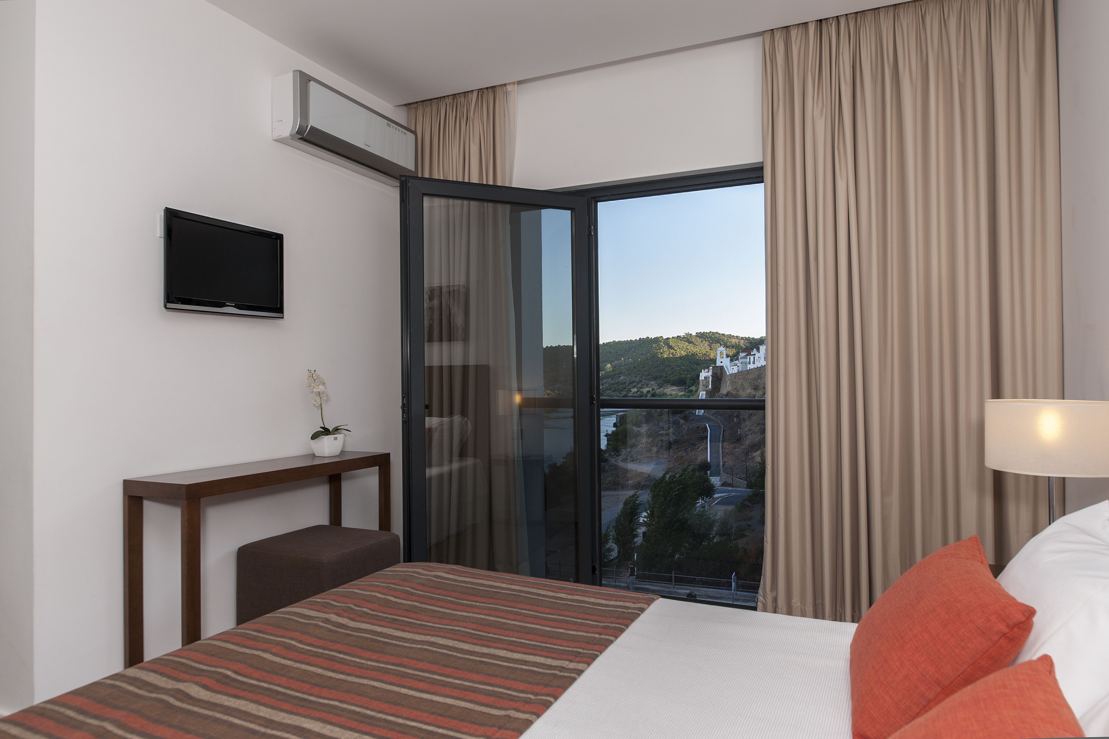 A hotel room with a bed, a desk, a TV, and a view of the outdoors.