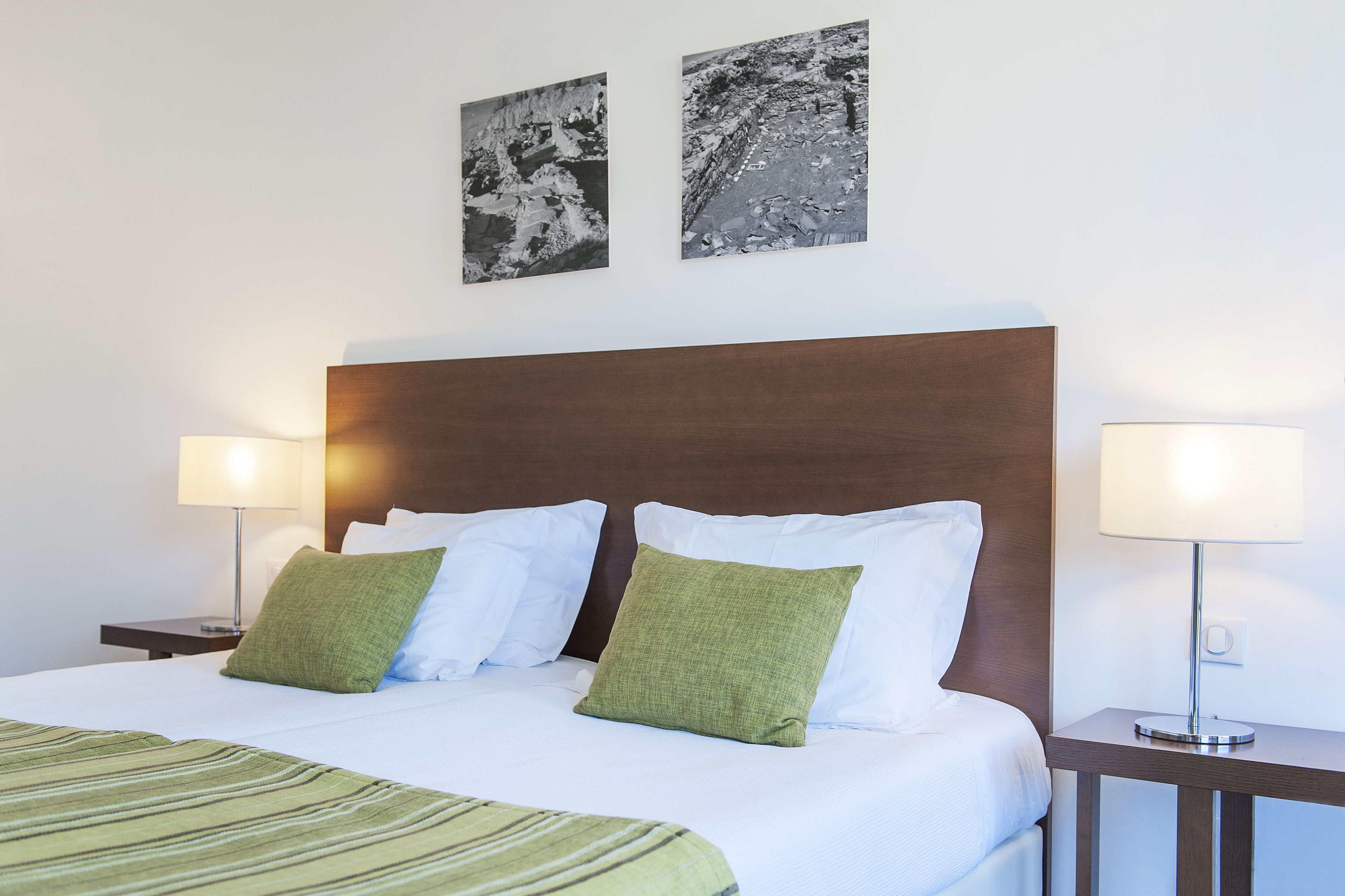 A neatly made bed with white and green pillows, a wooden headboard, and two bedside lamps.