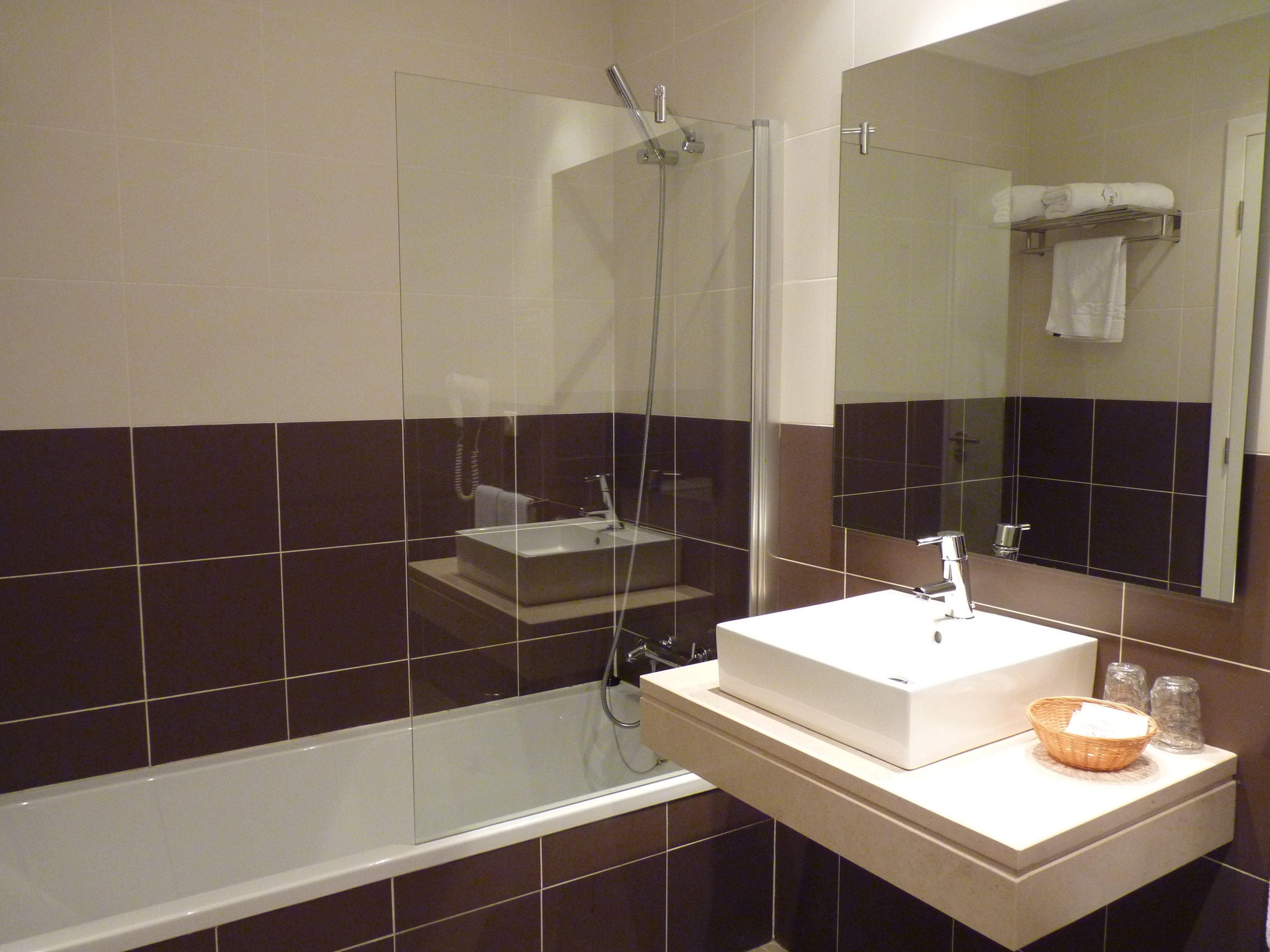 Un baño moderno con ducha envuelta en vidrio, un lavabo blanco y un espejo sobre él.